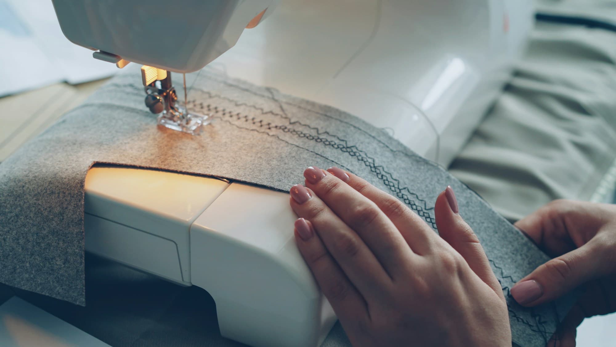 Hands guiding grey fabric through a sewing machine